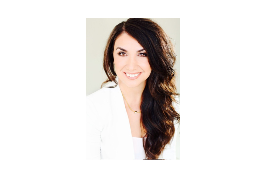 Professional woman with long dark hair smiling in a white blazer.